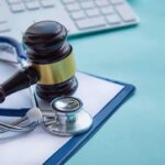 Gavel and stethoscope on medical clipboard near keyboard