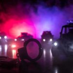 Gunfire Surges While Prosecutors Wait For Reinforcements Handcuffs on a surface with police cars and flashing lights in the background