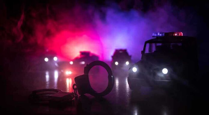 Handcuffs on a surface with police cars and flashing lights in the background