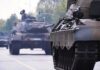Military tanks drive down a city street
