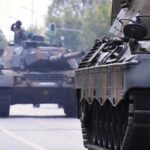 Military tanks drive down a city street