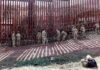 Soldiers install concertina wire along a tall border fence