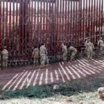 Soldiers install concertina wire along a tall border fence