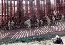 Soldiers install concertina wire along a tall border fence