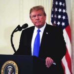 man at podium with microphone and US flag