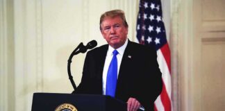 man at podium with microphone and US flag