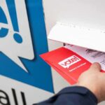 Hand inserting mail-in ballot envelope into drop box