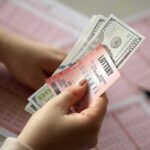 Hands holding lottery tickets and U.S. dollar bills