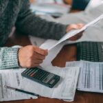 Person reviewing bills with calculator at cluttered desk