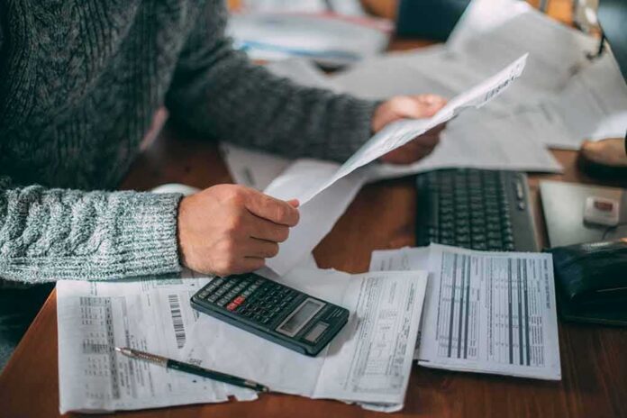 shutterstock_2232534015 Person reviewing bills with calculator at cluttered desk