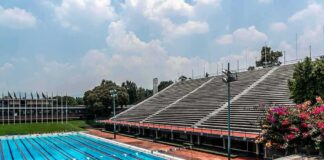 Olympic-size outdoor swimming pool beside empty stadium bleachers