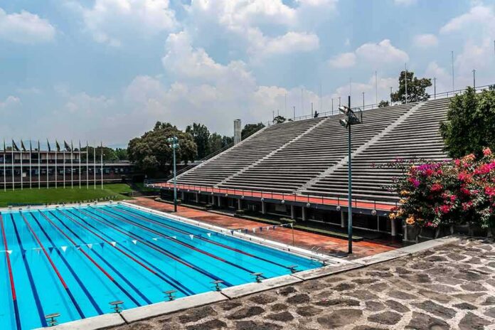 Olympic-size outdoor swimming pool beside empty stadium bleachers