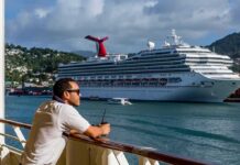 Man leaning on ship railing looking at a docked cruise ship