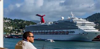Man leaning on ship railing looking at a docked cruise ship