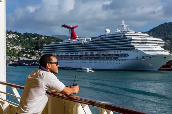 shutterstock_775617838 Man leaning on ship railing looking at a docked cruise ship