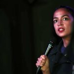 A Progressive Comeback Faces Familiar Headwinds Woman speaking into a microphone on stage