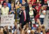 politician on stage at a rally raising a fist amid cheering crowd