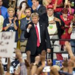 The GOP Is Rewriting the Midterm Playbook politician on stage at a rally raising a fist amid cheering crowd