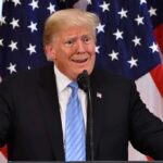 man at podium with U.S. flags behind him