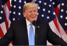 man at podium with U.S. flags behind him