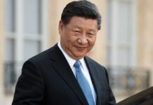 Xi Jinping in a dark suit with a blue tie, smiling outdoors