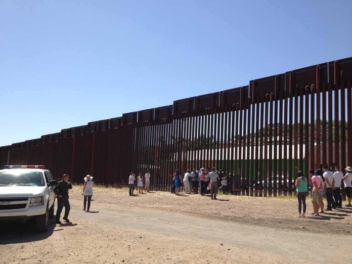 shutterstock_1423702385 Border fence with group of people and a patrol vehicle