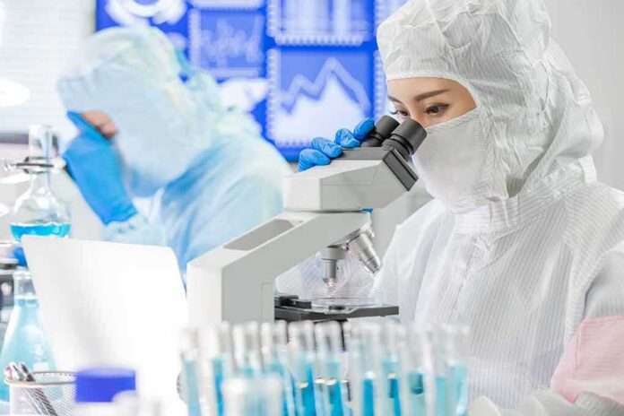 Scientist in protective suit using a microscope