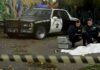 Crime scene with police car and two investigators by a covered body