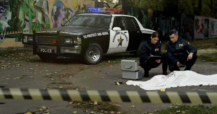 shutterstock_1709493973 Crime scene with police car and two investigators by a covered body
