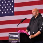 Democrat Dares His Own Party To Keep This Up man at podium speaking with US flag backdrop