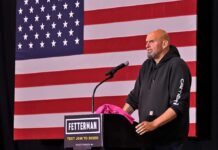 man at podium speaking with US flag backdrop