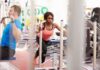 Woman performing sled push in a gym beside a man using a cable machine