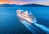 Cruise ship sailing at sunset near mountainous coastline