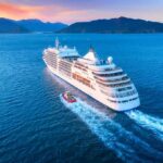 Fuel Shock Strands Luxury Nomads Cruise ship sailing at sunset near mountainous coastline