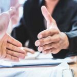 Two people extending hands for a handshake across a desk