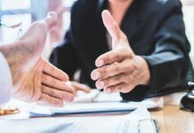 Two people extending hands for a handshake across a desk