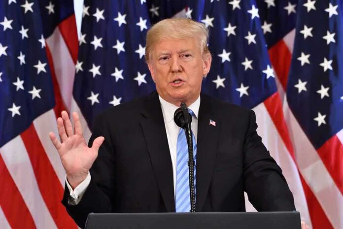 shutterstock_1198949239 Donald Trump speaking at a podium with American flags behind him