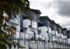 Homeowners Score Big – Cities Panic Modern townhouse row with glass balconies and metal accents under cloudy sky