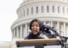 Woman in hijab speaking at podium with microphones