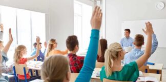 Students raise hands in a classroom with a teacher at the front