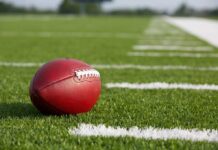Betting Whispered, Brawl Explodes At Kids’ Game A red American football resting on a green artificial turf field