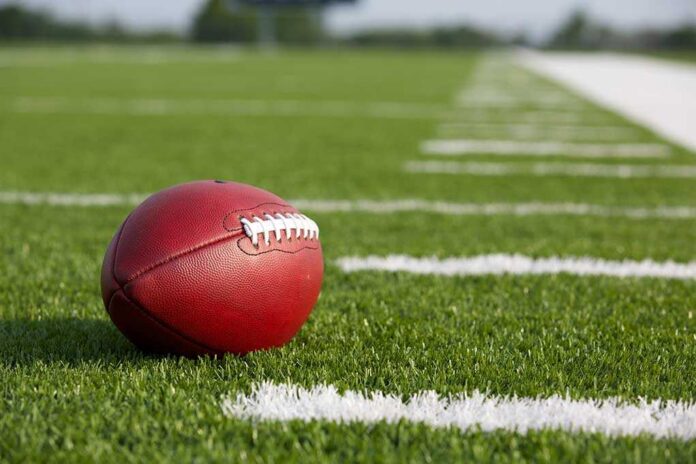 Pro,American,Football,On,The,Field,With,Room,For,Copy A red American football resting on a green artificial turf field