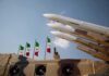 Warships Named – Retaliation Incoming? Missile launchers on a military vehicle with flags in the background