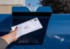 Hand mailing an envelope into a blue postal box