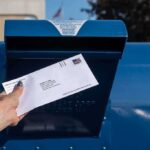 Hand mailing an envelope into a blue postal box