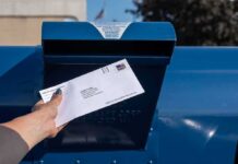 Hand mailing an envelope into a blue postal box