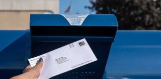 Hand mailing an envelope into a blue postal box