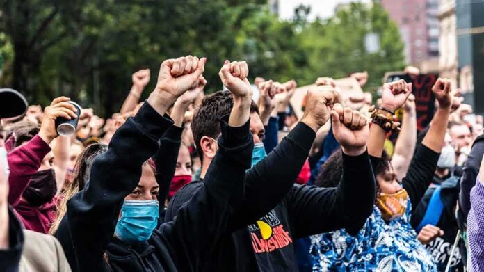 Crowd of protesters with raised fists wearing masks