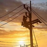 Utility workers on power poles at sunset