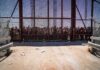 Crowd stands behind tall metal fence at border crossing